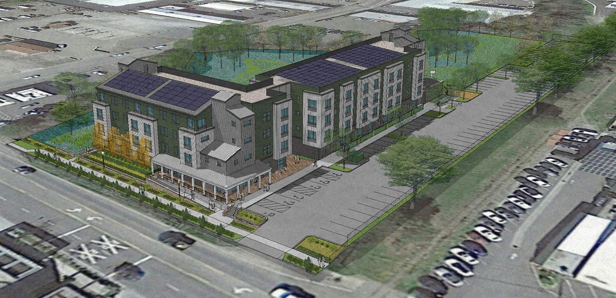 Aerial view of a modern multi-story building complex with parking lots and solar panels on the rooftops, surrounded by greenery and adjacent roads.